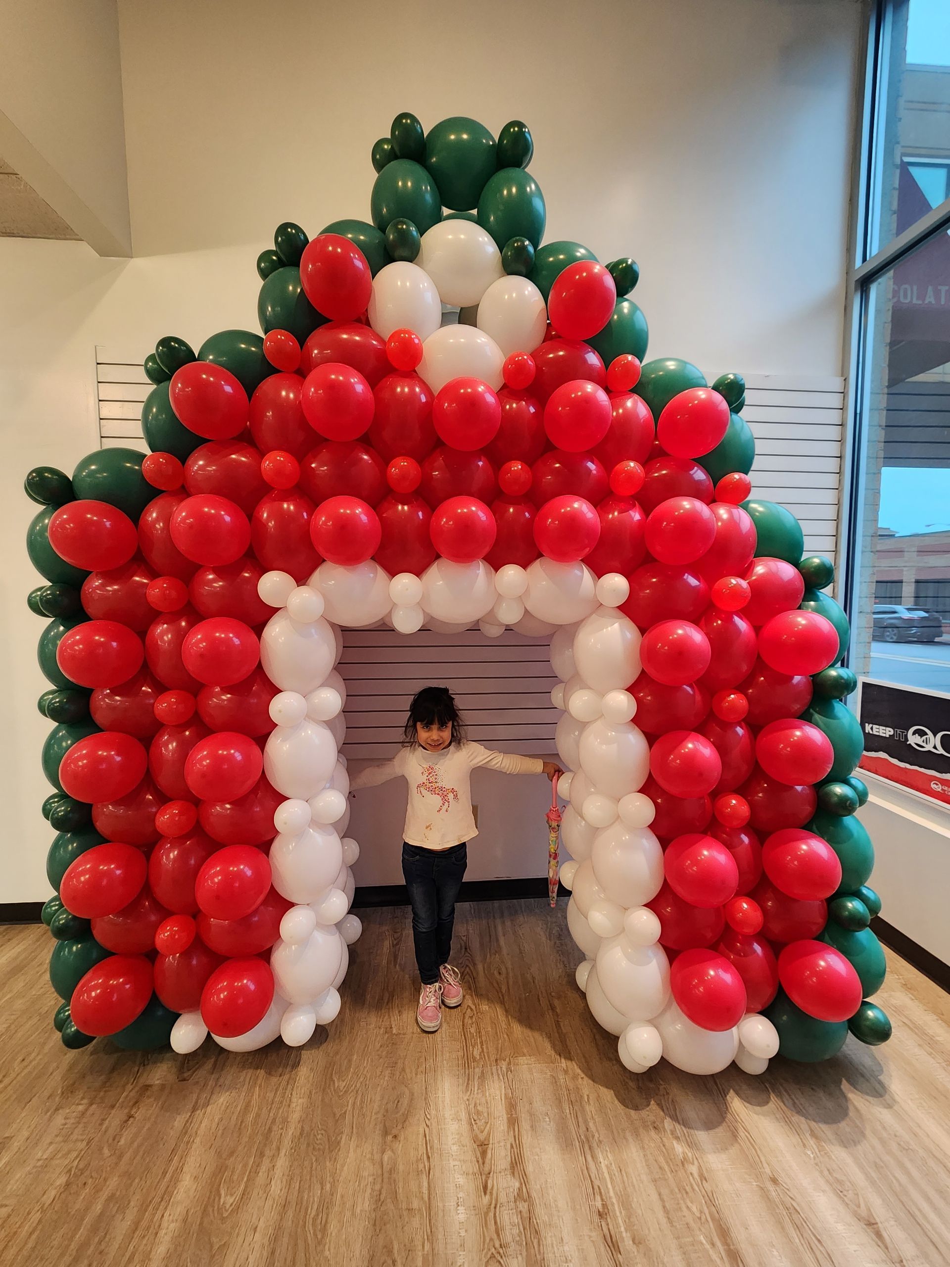 A little girl is standing in front of a christmas balloon arch.
