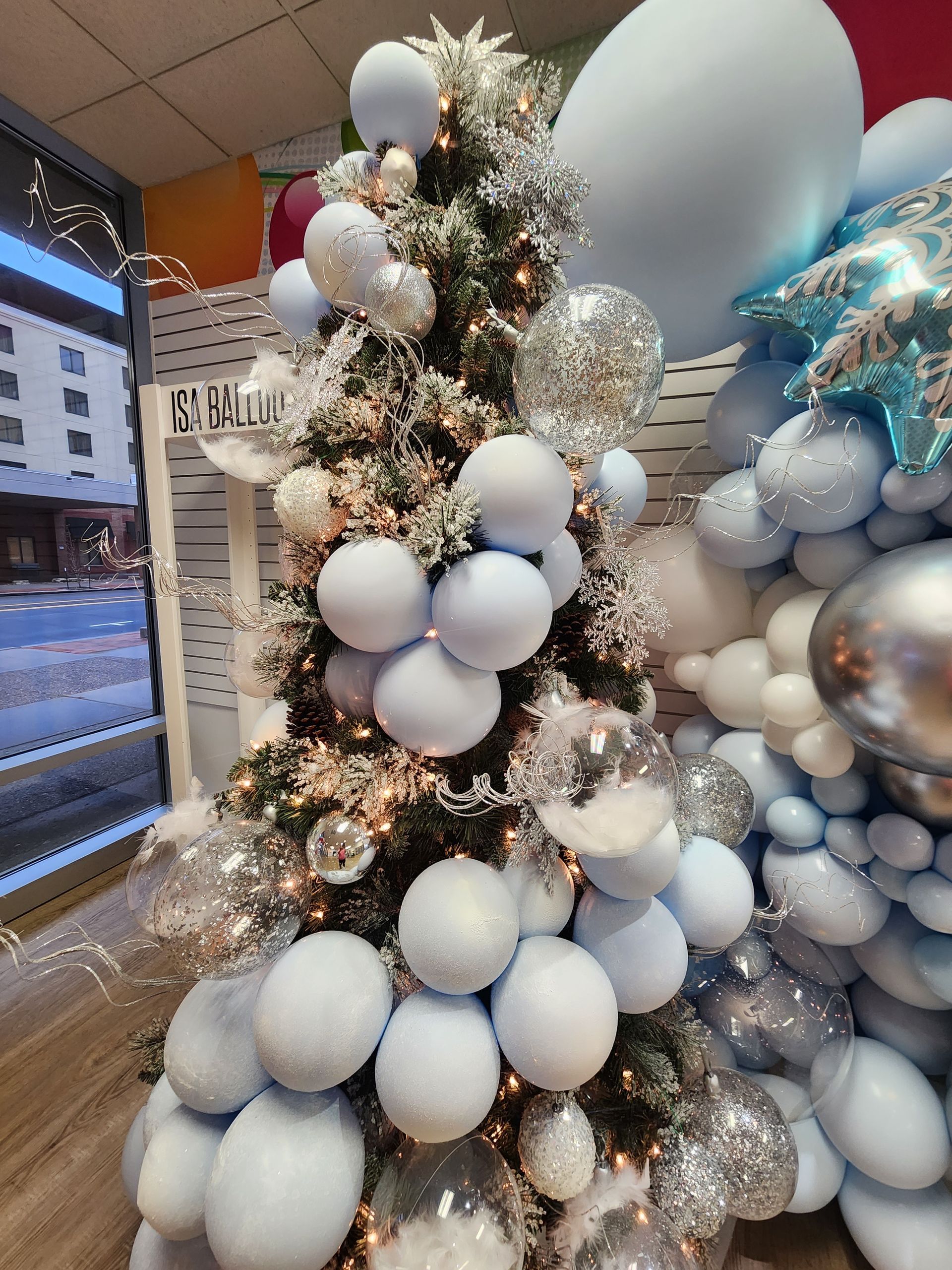 A christmas tree is decorated with blue and silver balloons.
