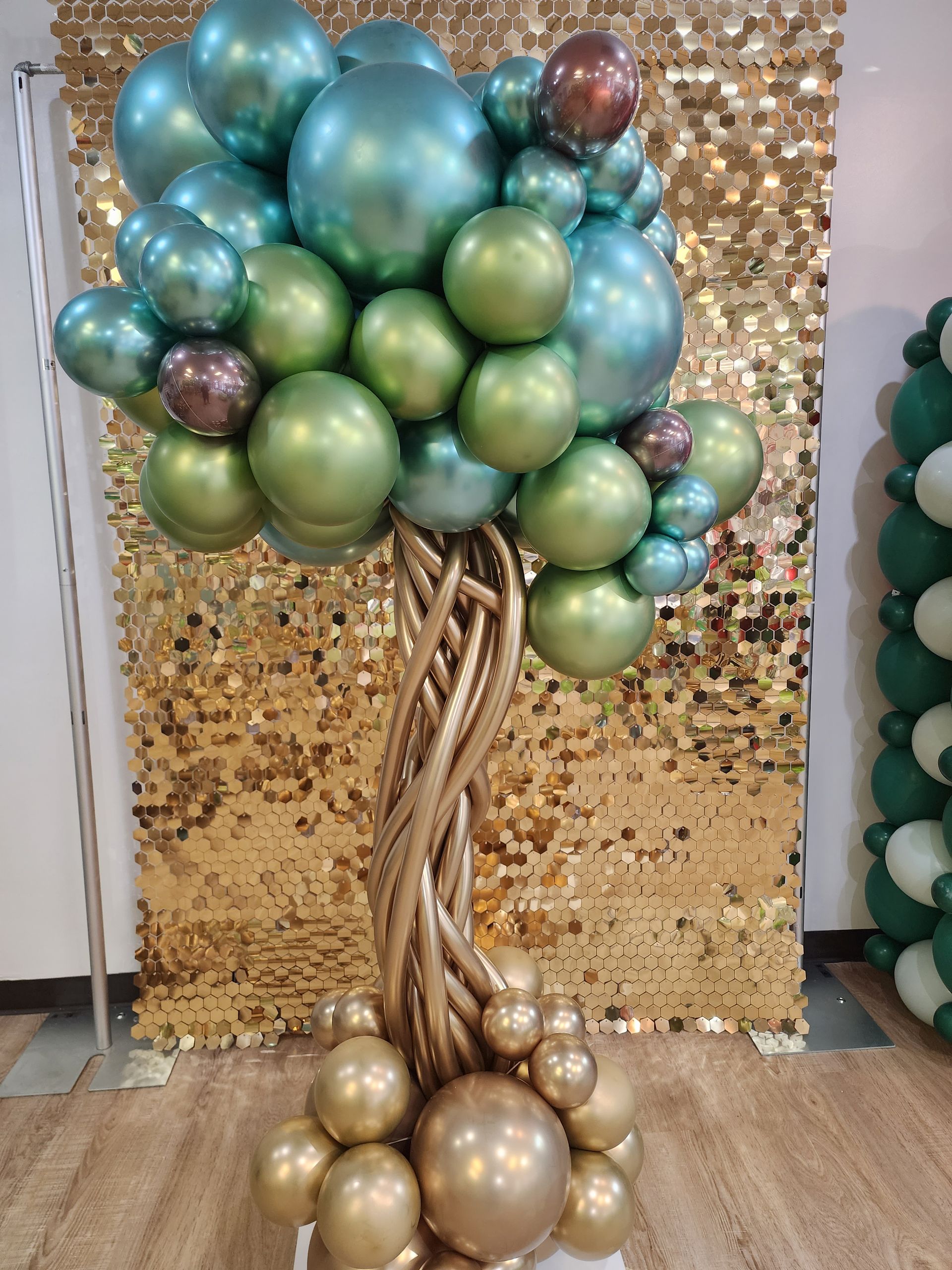 A tree made of balloons is sitting in front of a gold wall.