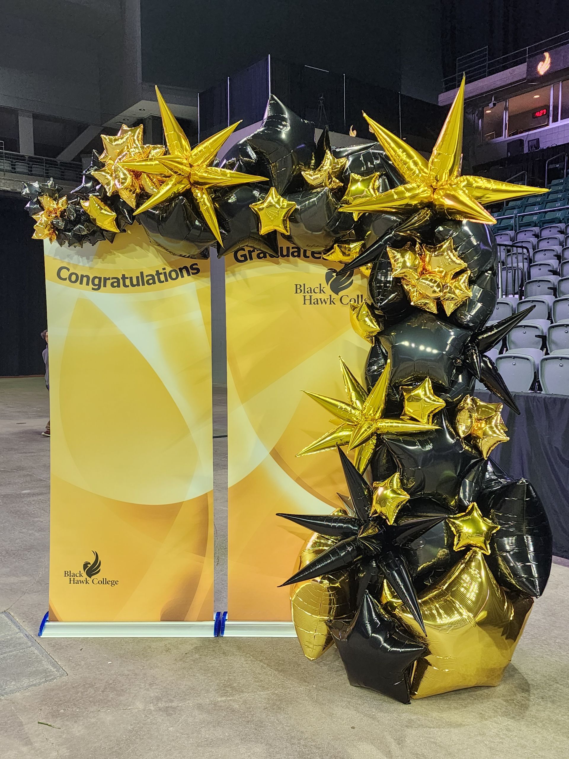 A sign that says congratulations is surrounded by black and gold balloons.