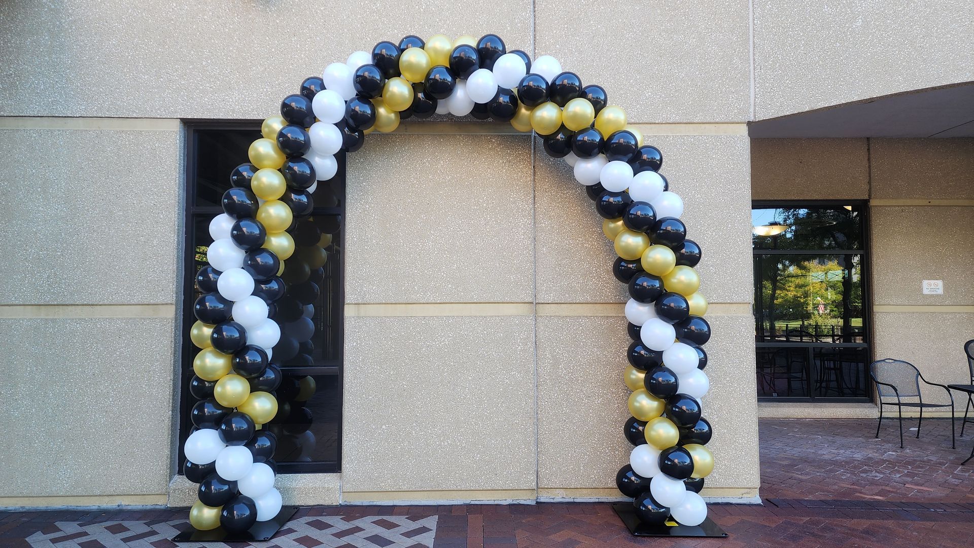 A black and gold balloon arch is sitting in front of a building.