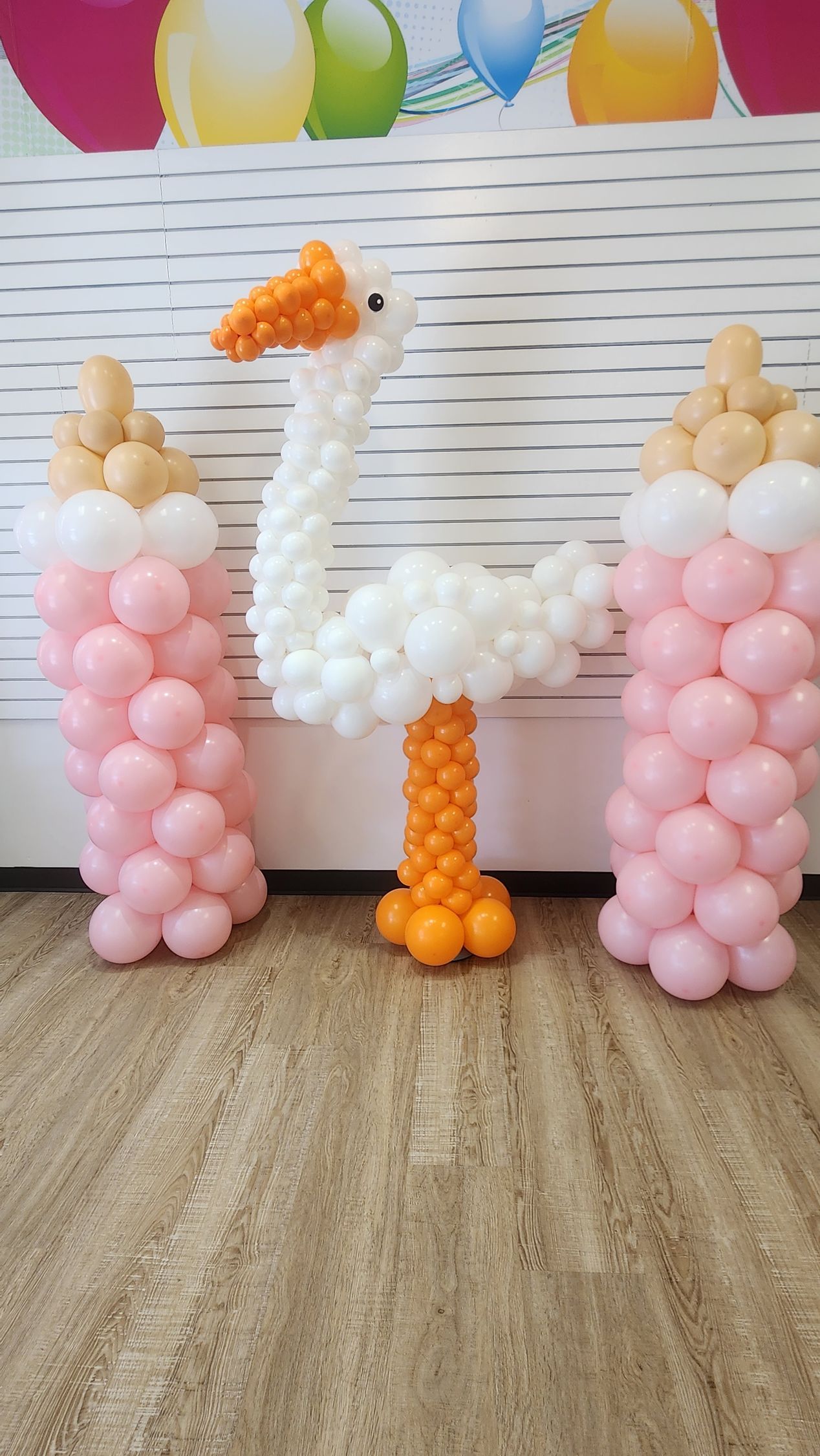 A stork made out of balloons is standing next to a baby bottle.