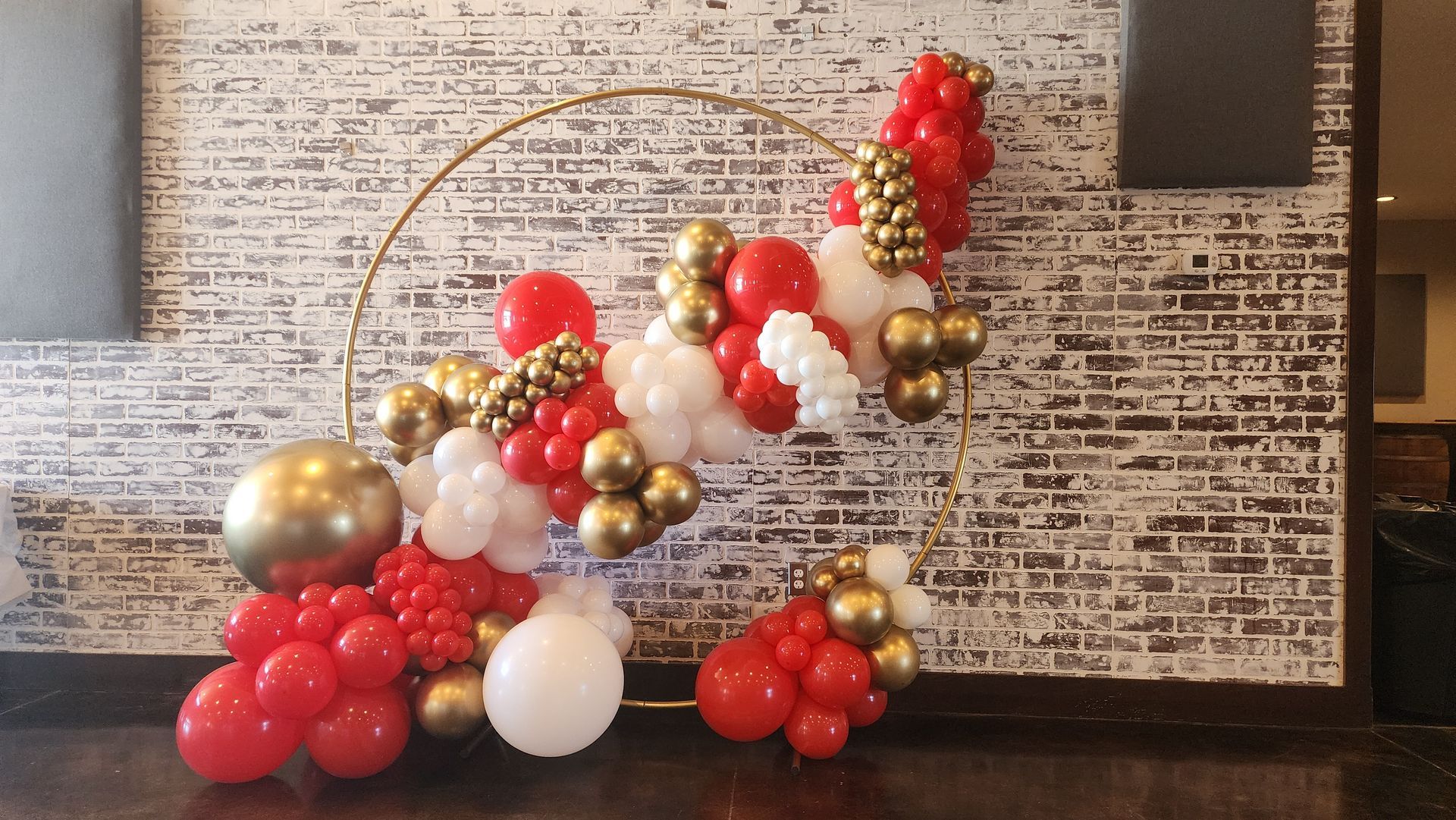 A bunch of red , white and gold balloons are sitting in front of a brick wall.