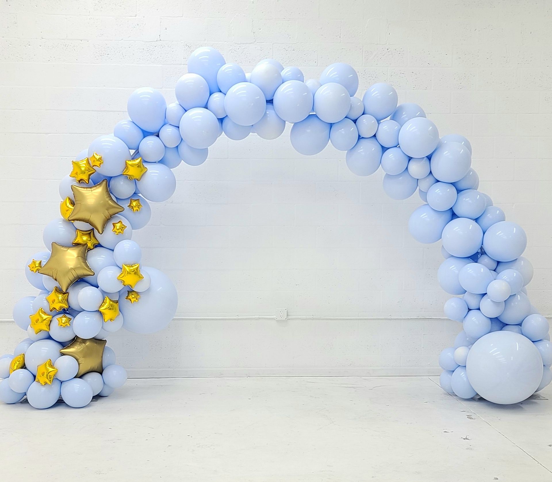 A blue balloon arch with gold stars on a white wall.