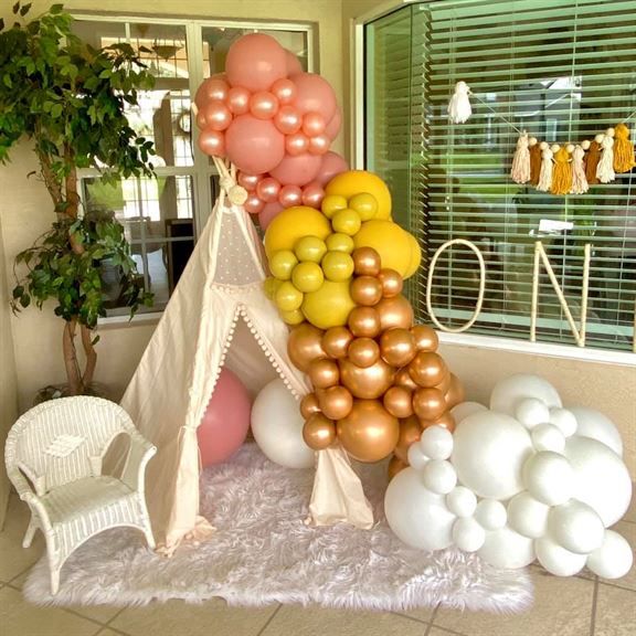 A teepee is surrounded by balloons in front of a window that says one