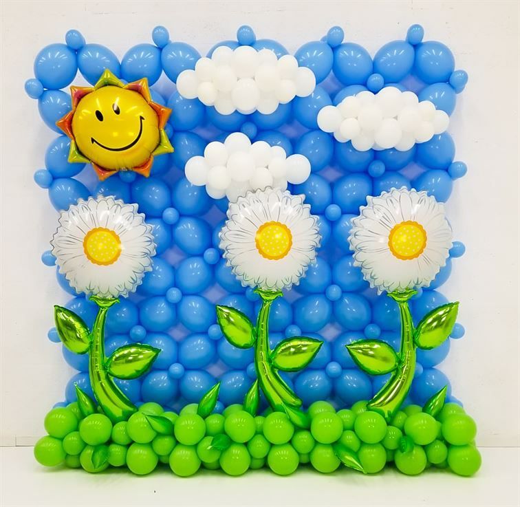 A wall made of blue and green balloons with flowers and clouds