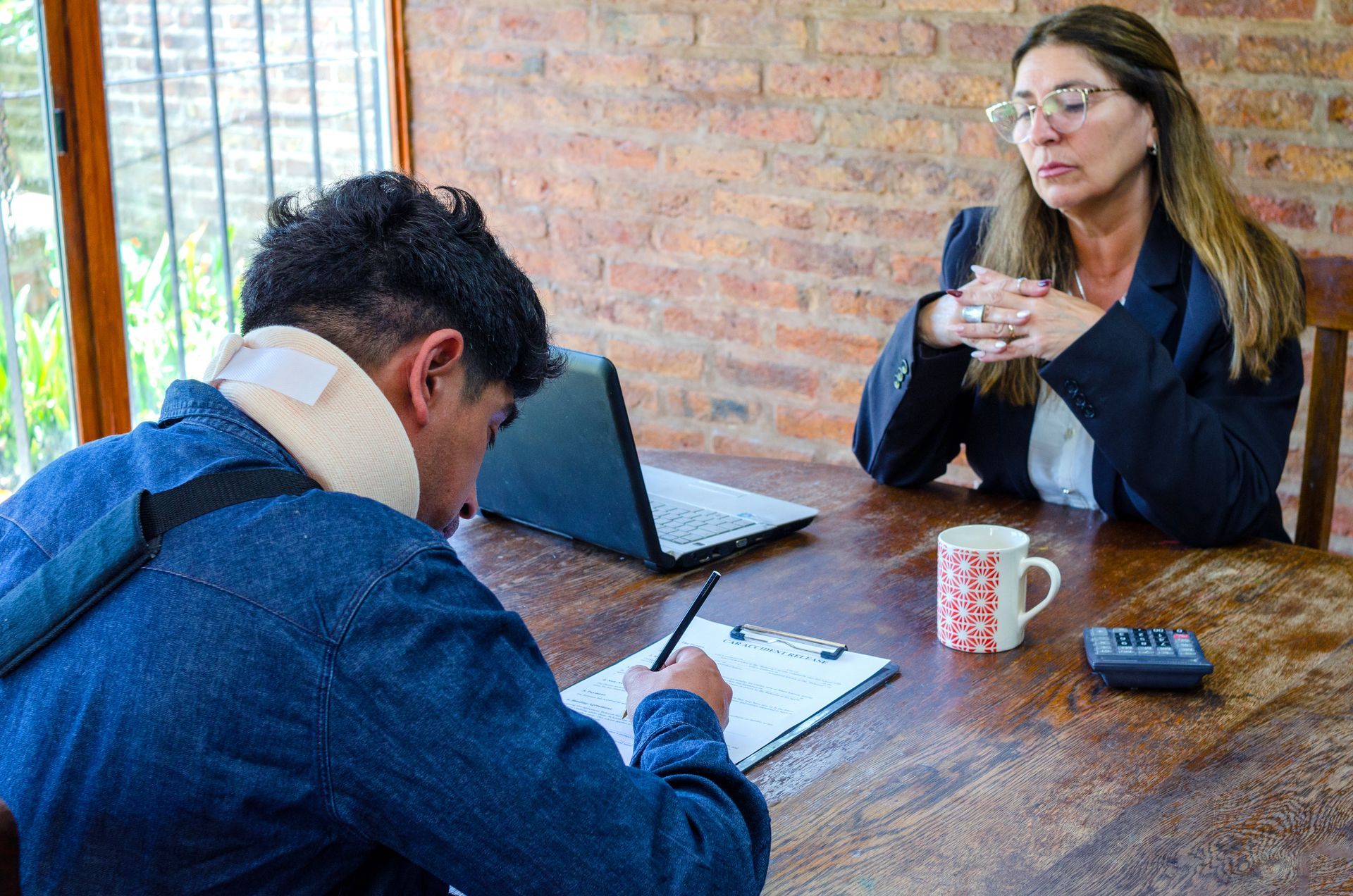 An injured man in a neck brace filling out paperwork at a table across from a female lawyer