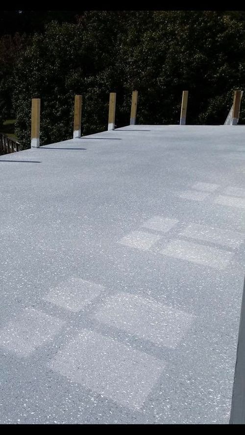 Light gray flat roof with white skylight patches and short wooden posts along the edge near trees.