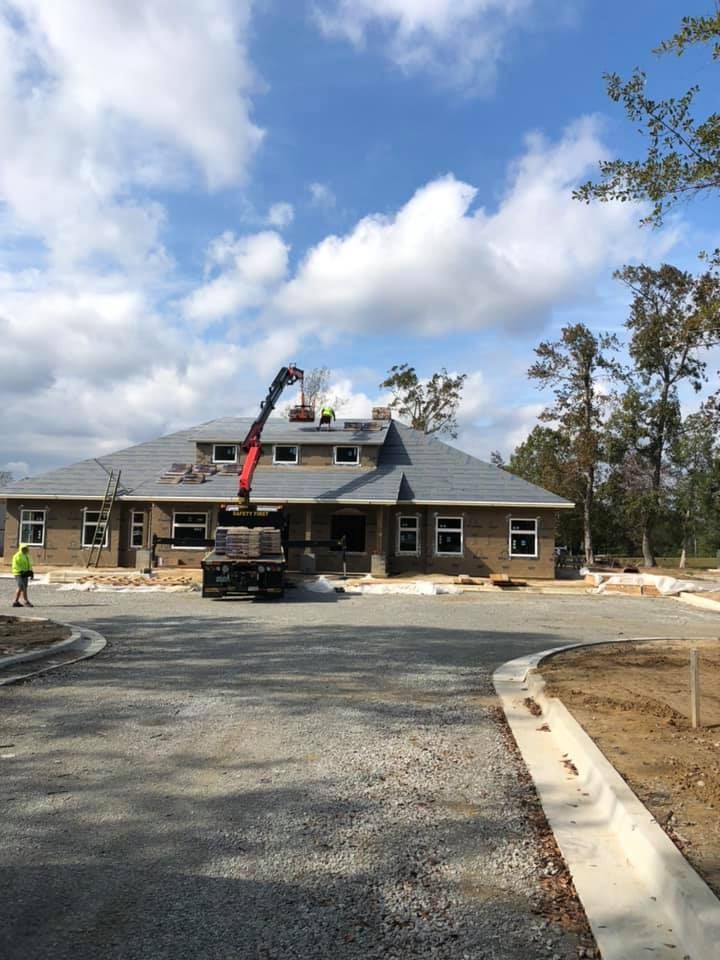 Construction crew finishing a brick house with crane and gravel driveway under a cloudy sky