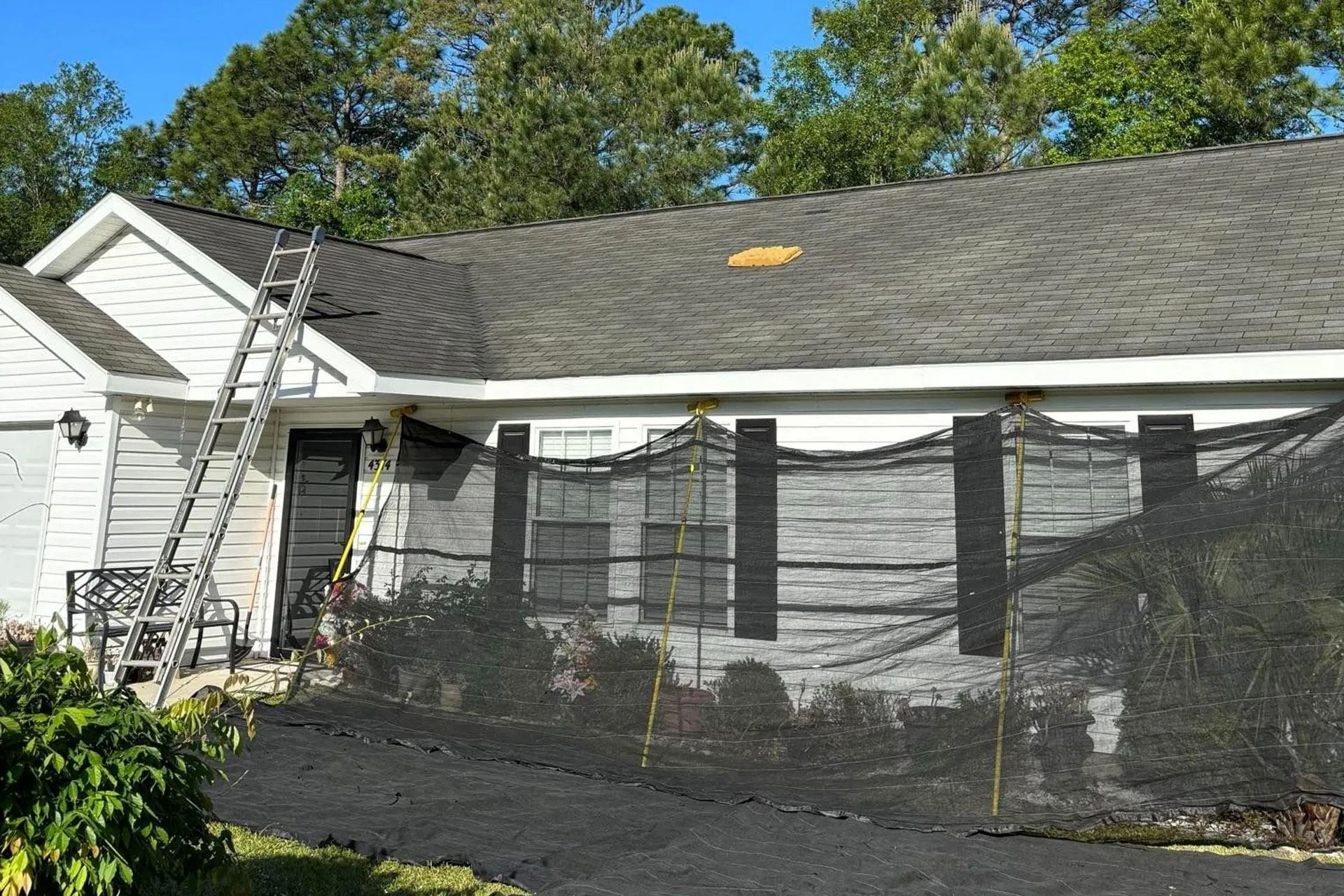 White house with a ladder on the roof and black netting over the front porch area.