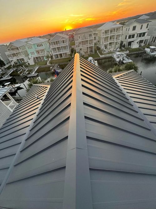 Sunset over apartment buildings, viewed from a rooftop with a metal ridge in the foreground