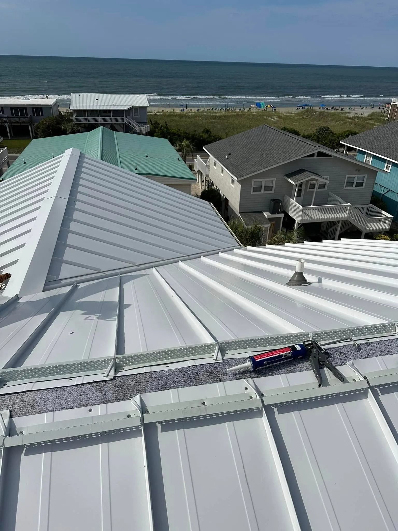 Rooftops with gray metal roofs overlooking a grassy coast and ocean under a cloudy sky.