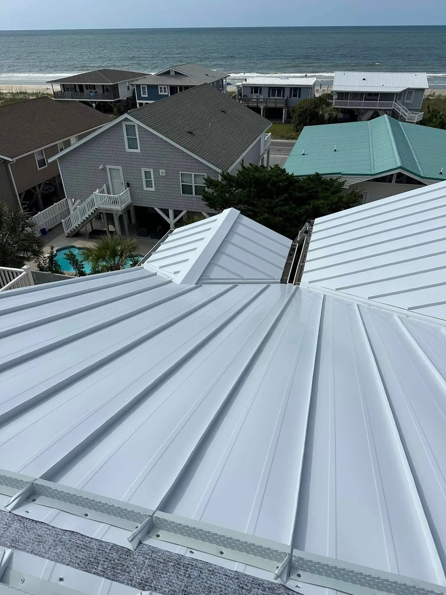 Rooftop view of beach houses with metal roofs and the ocean in the background