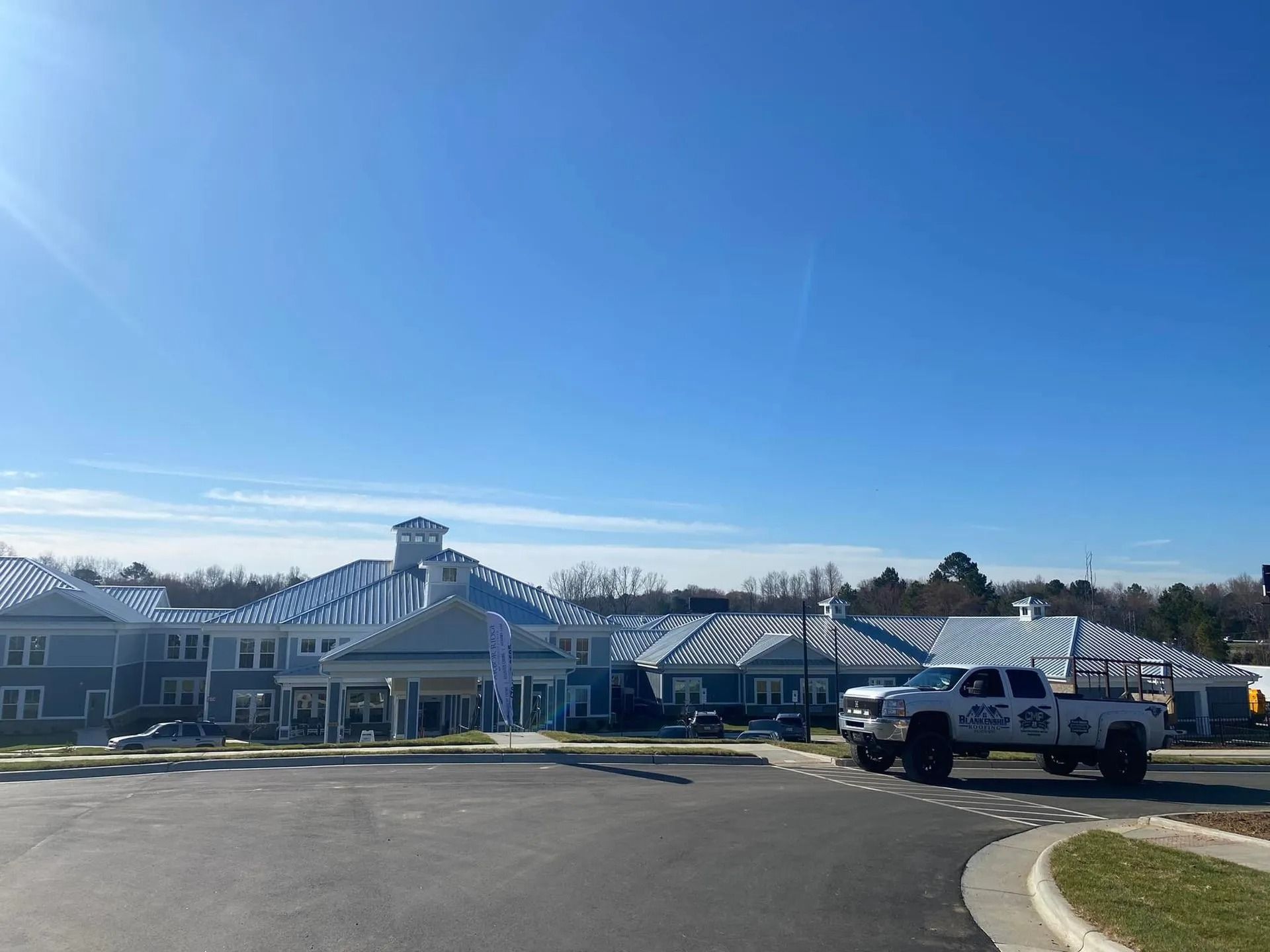 Large white building with a cupola under a clear blue sky, with parked trucks in front.