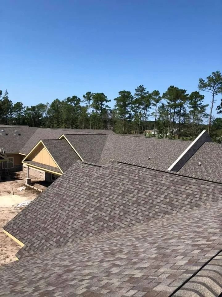 Newly installed brown shingle roof on a house under a clear blue sky, with trees in the background