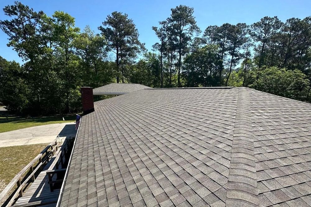 Shingled roof viewed from above, with trees and blue sky in the background