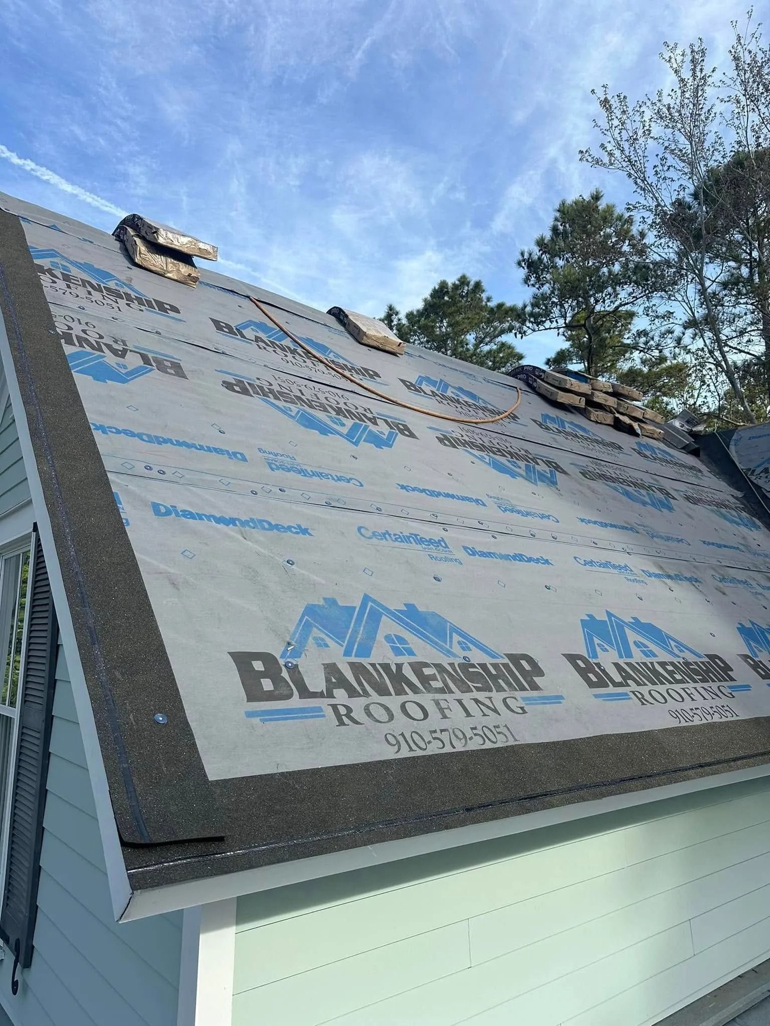 Roof under repair with black roofing underlayment and blue printed branding under a blue sky.