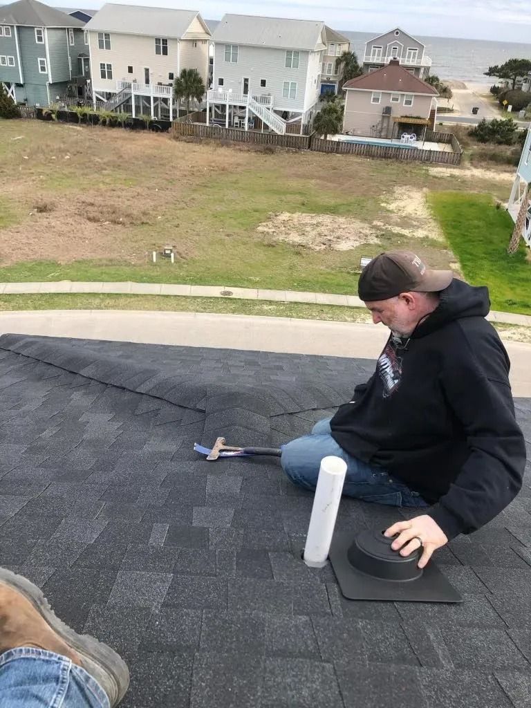 Person sitting on a roof with a drink cup, overlooking a grassy hillside and houses below.