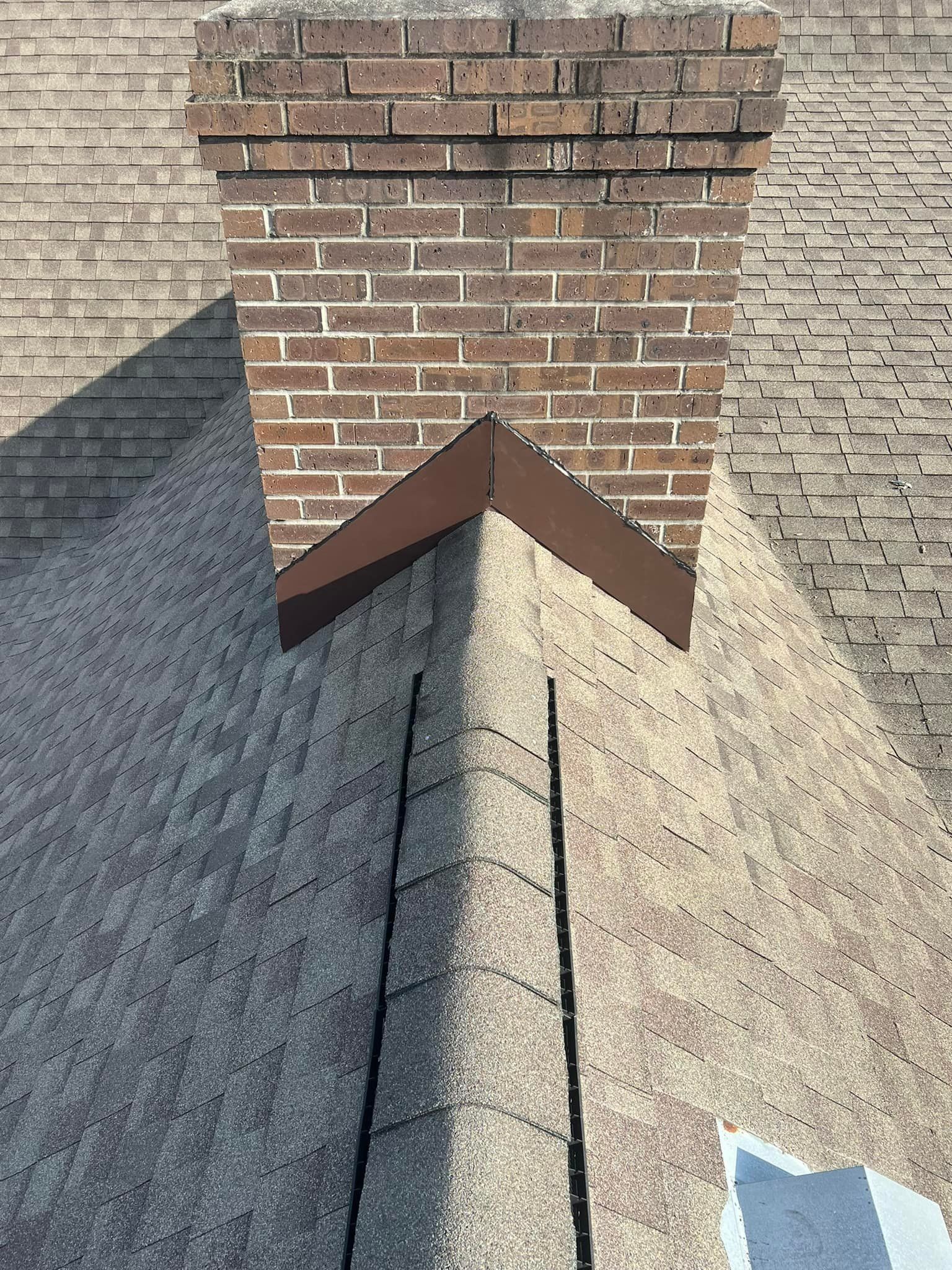 Brick chimney with a metal flashing and vent on a shingled roof against a light exterior wall