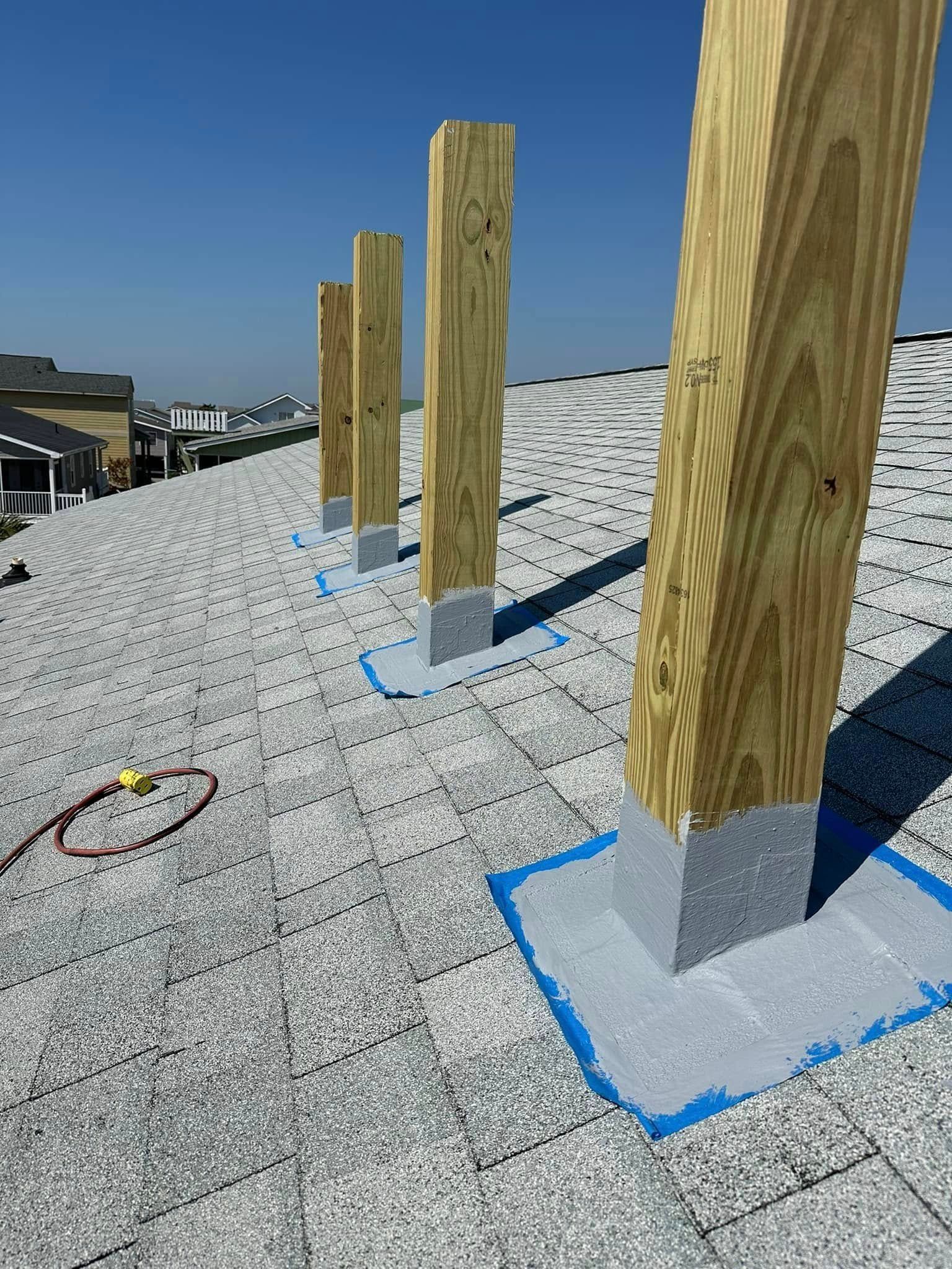 Wooden roof posts anchored in gray concrete on a gravel-covered rooftop, with blue tape markings.