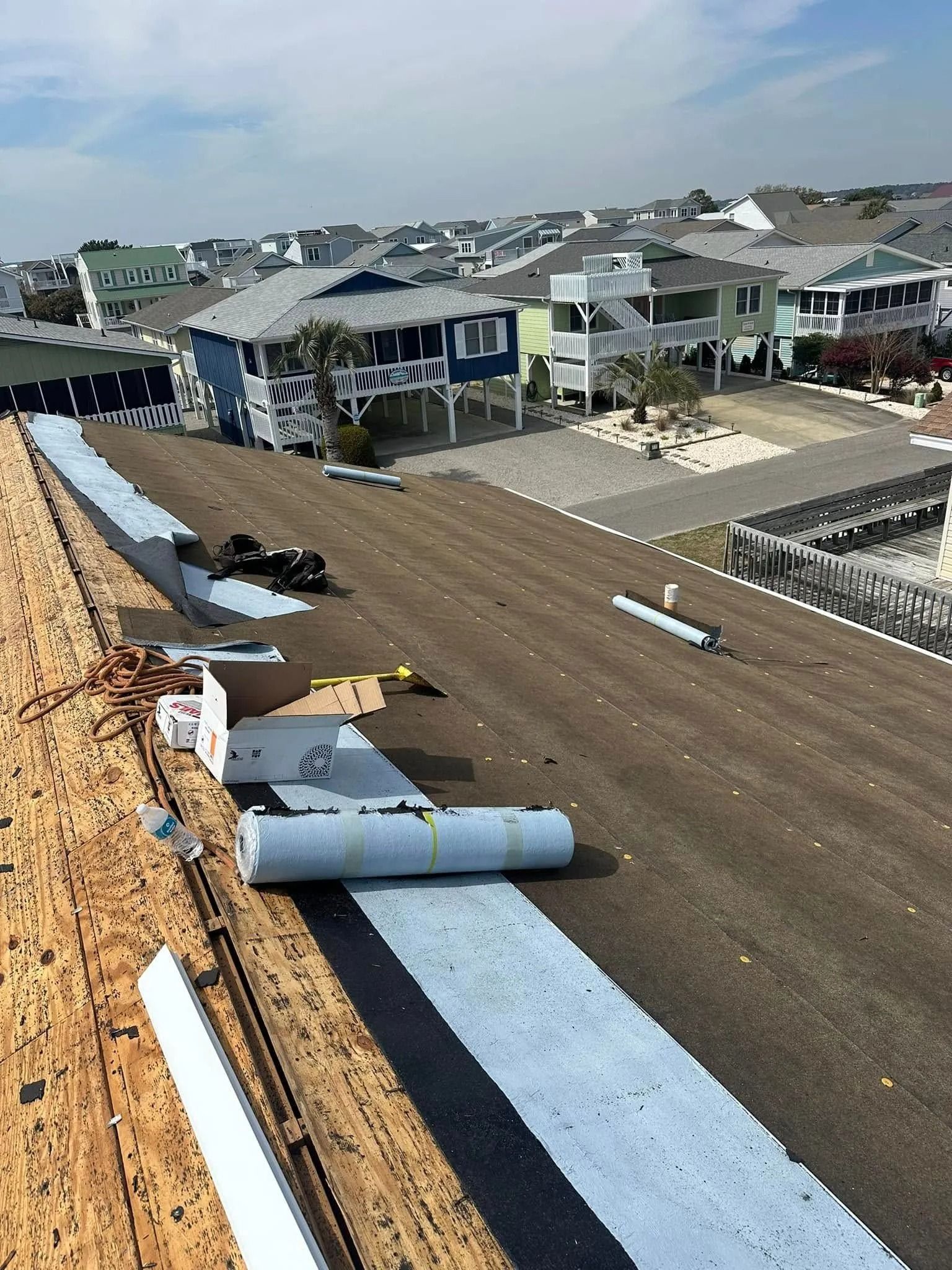 Roof under construction with rolled roofing materials on a sloped rooftop in a residential neighborhood