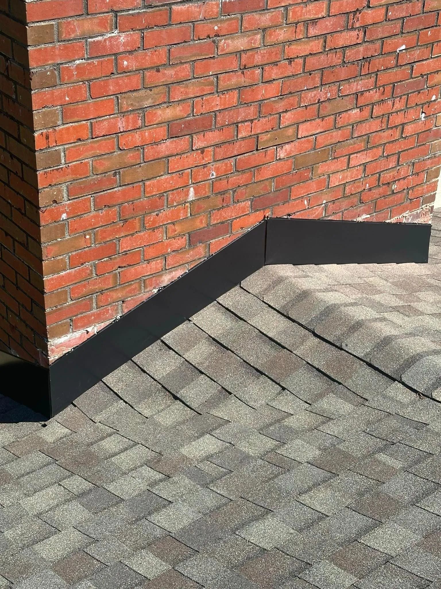 Brick wall with black flashing above a gray shingled roof corner.