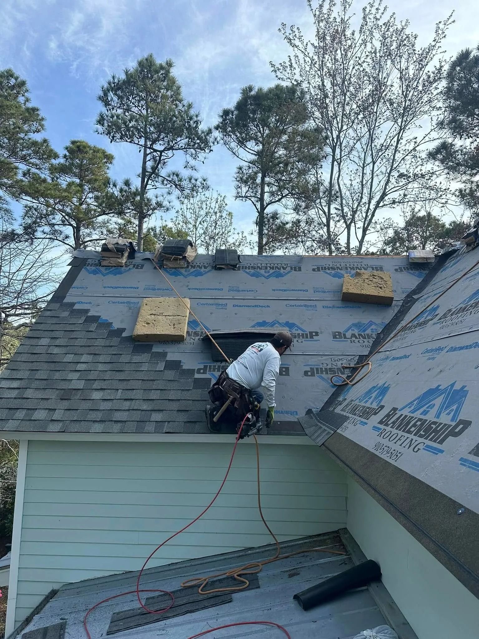 Worker installing roof shingles on a house with shingles and tools visible nearby.