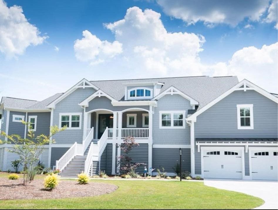 Gray suburban house with white trim, front porch, and two-car garage under a bright blue sky