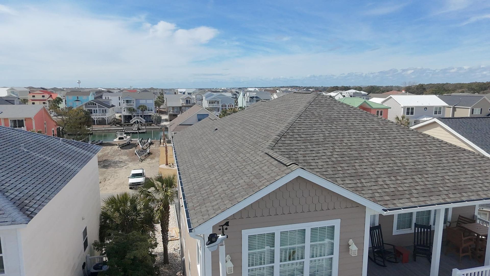 Suburban neighborhood rooftops under a blue sky, viewed from above.