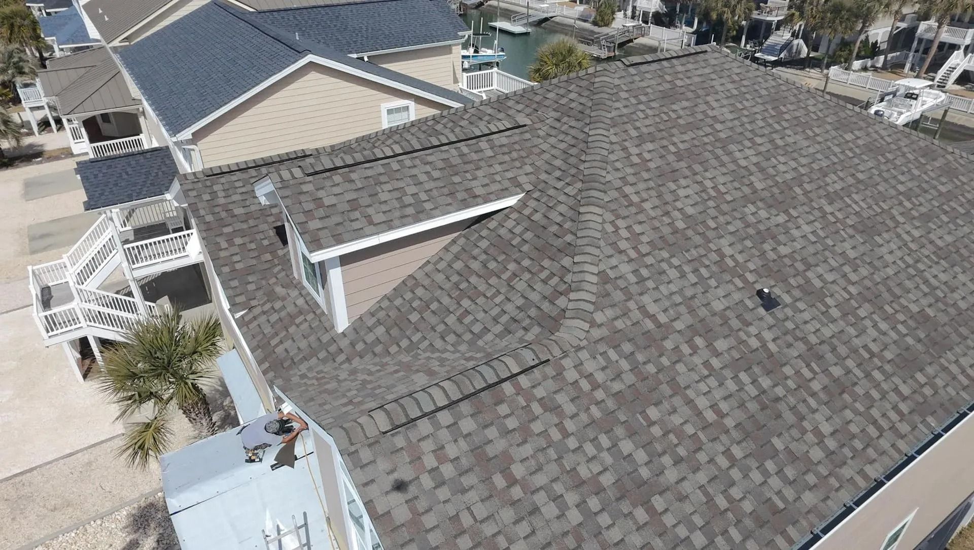 Aerial view of a suburban house with a gray shingle roof and neighboring homes.