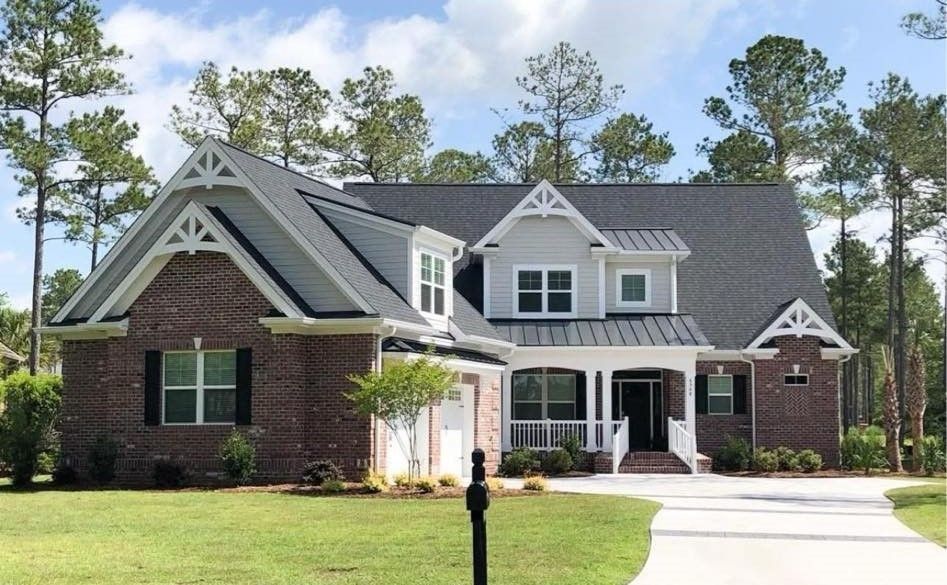 Two-story brick house with gray roof, white trim, and a front lawn under a clear sky