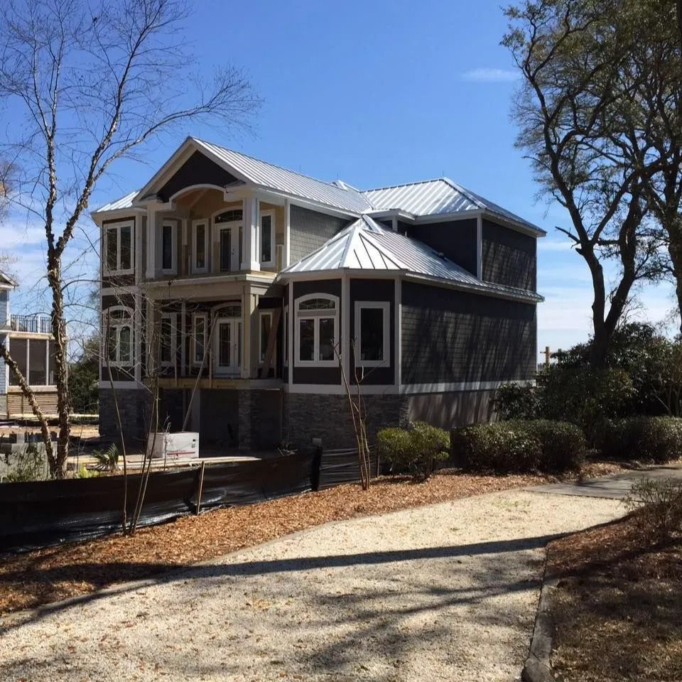 Victorian-style house with wraparound porch and metal roof on a sunny day