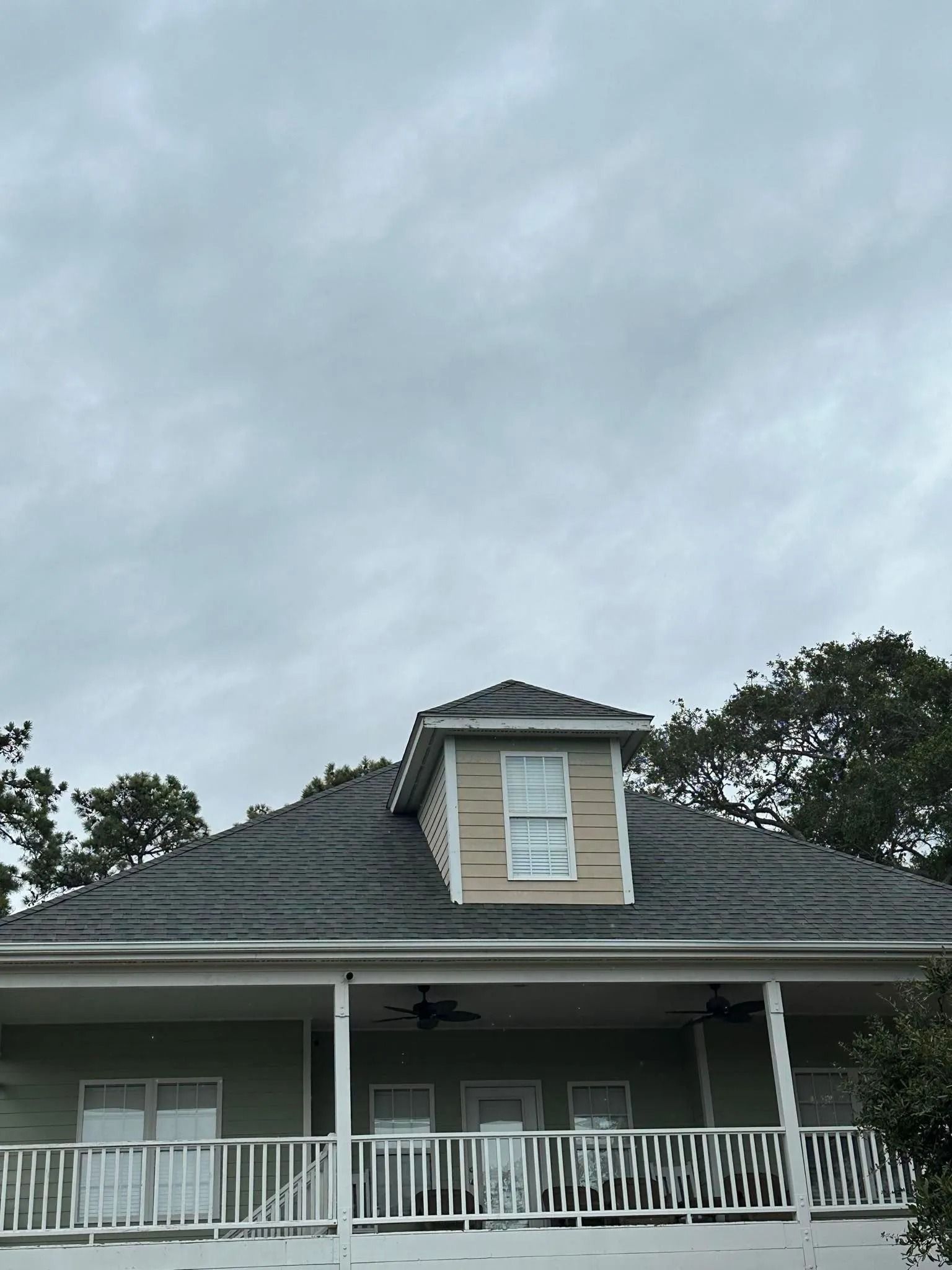 House exterior with gray roof, white porch railings, and a dormer under a cloudy sky