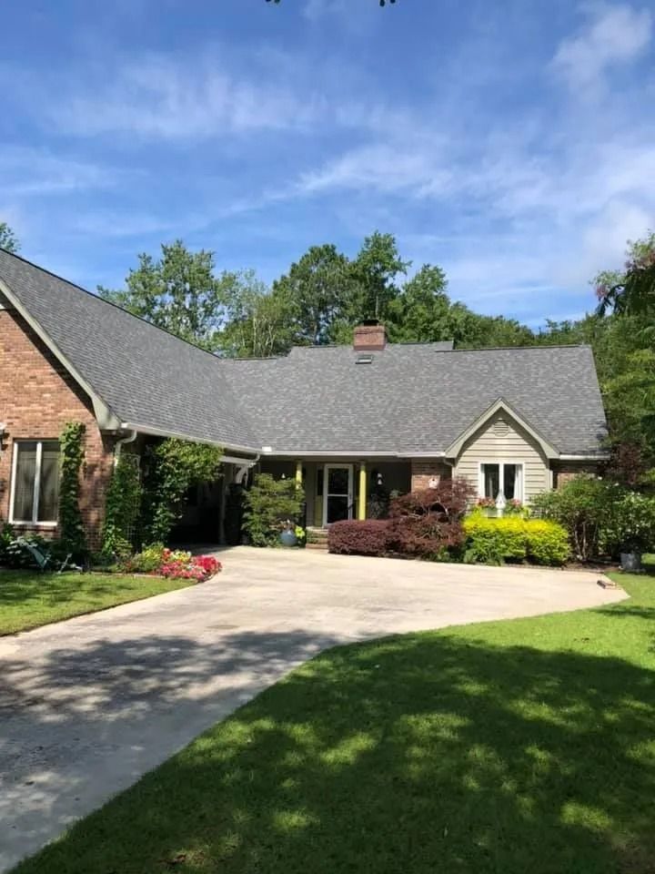Suburban brick house with gray roof, curved driveway, and green lawn under a blue sky