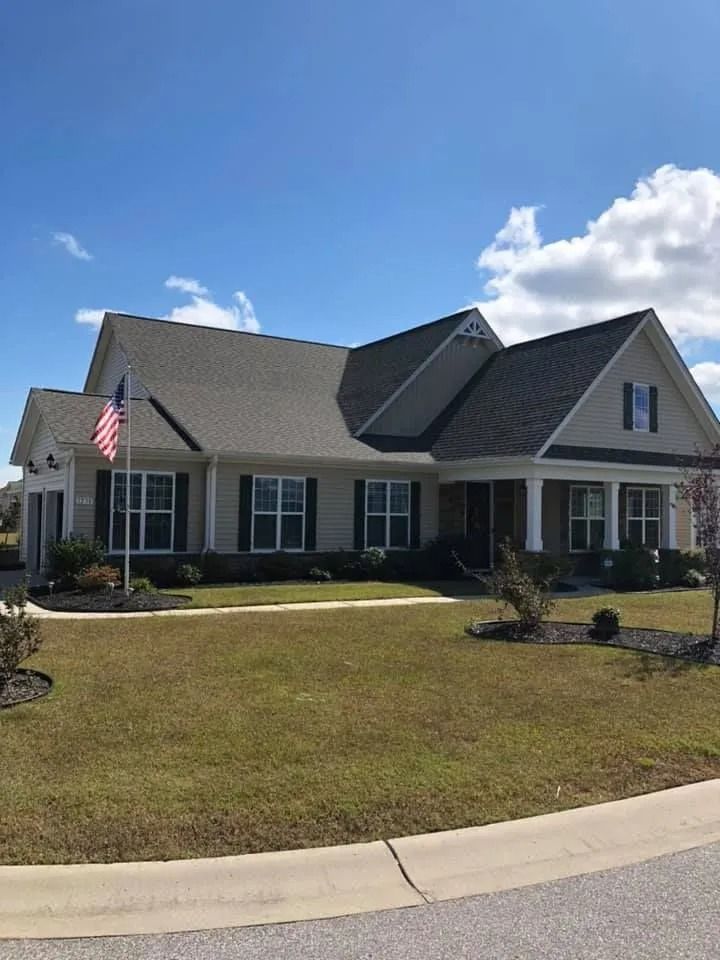 Single-story suburban house with gray roof, white trim, American flag, and a front lawn under a blue sky