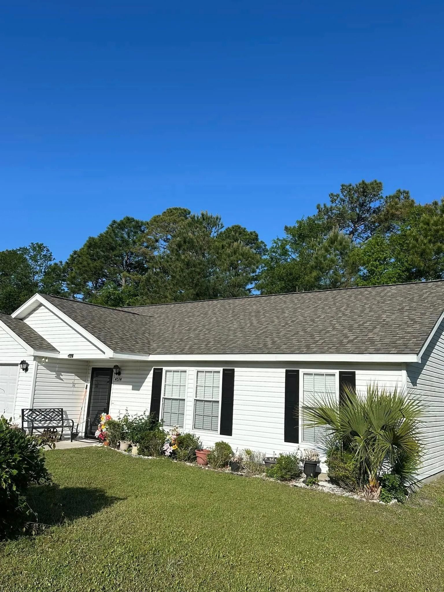 Single-story white house with gray roof and green lawn under a clear blue sky