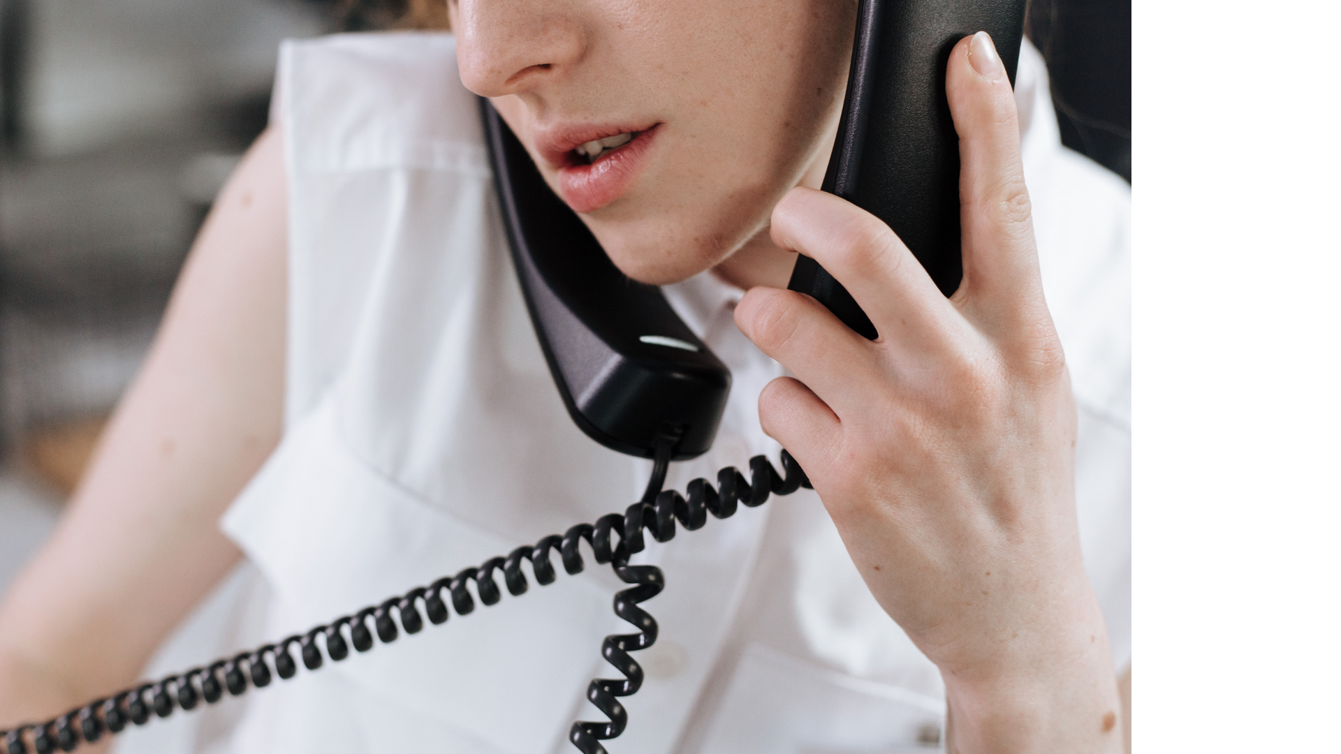 Woman in white shirt on a black landline phone, talking.
