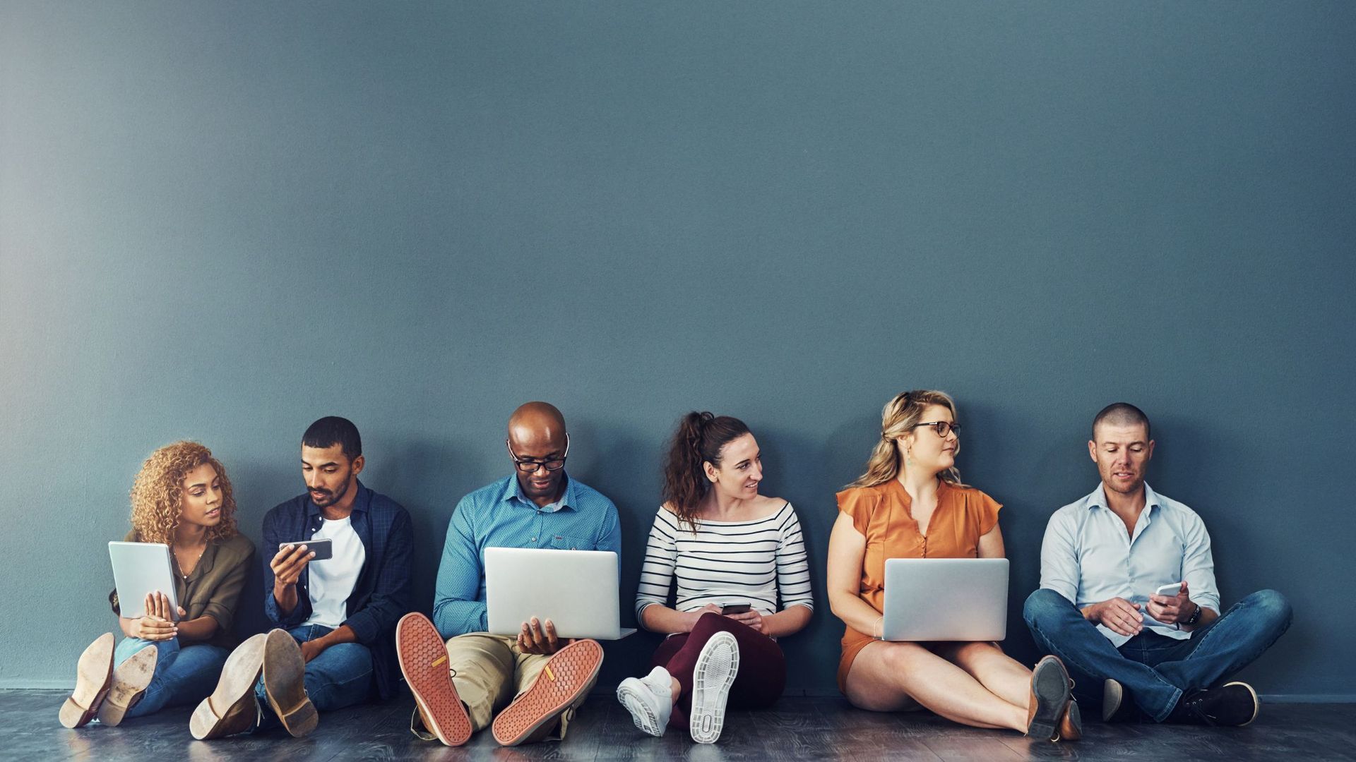 A group of people are sitting on the floor using laptops.