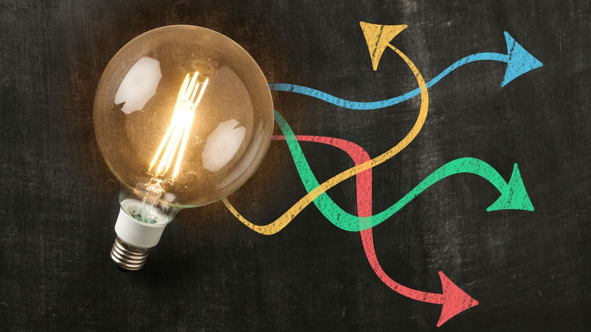 A light bulb is sitting on a blackboard with arrows drawn on it.