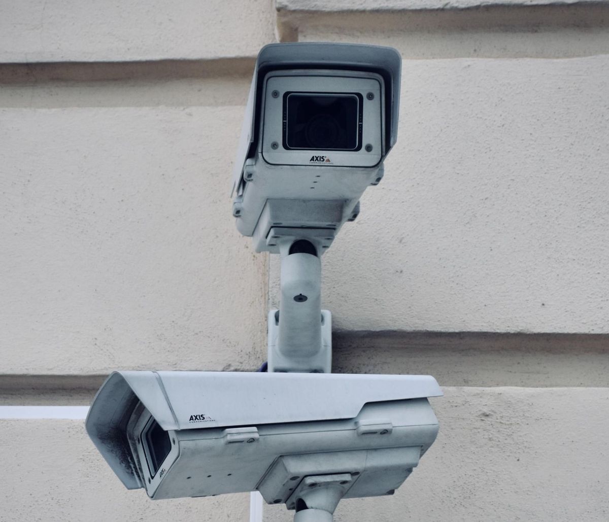 Two white security cameras mounted on a light-colored wall. One is top-facing, the other bottom-facing.