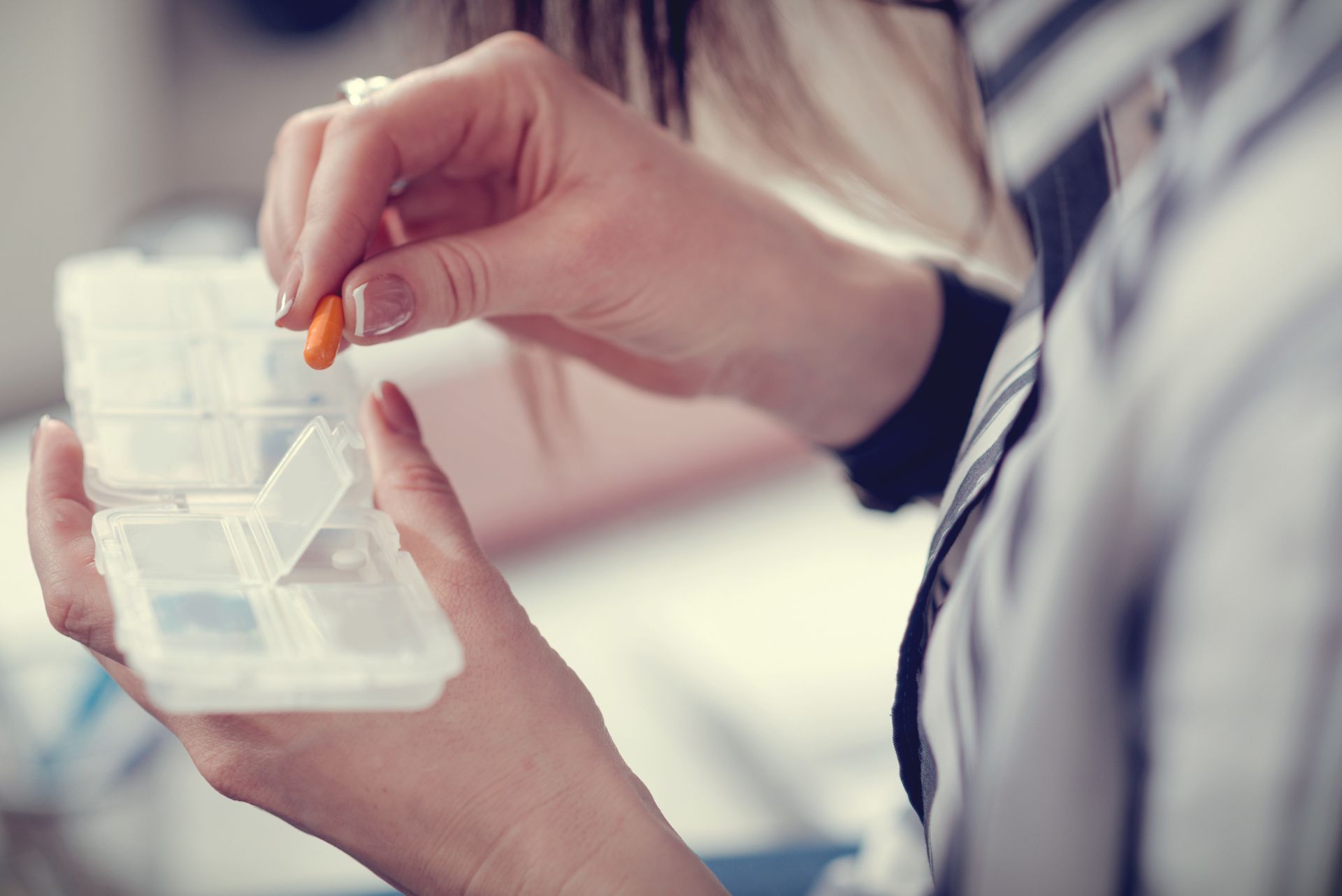 A woman is taking a pill out of a pill organizer.