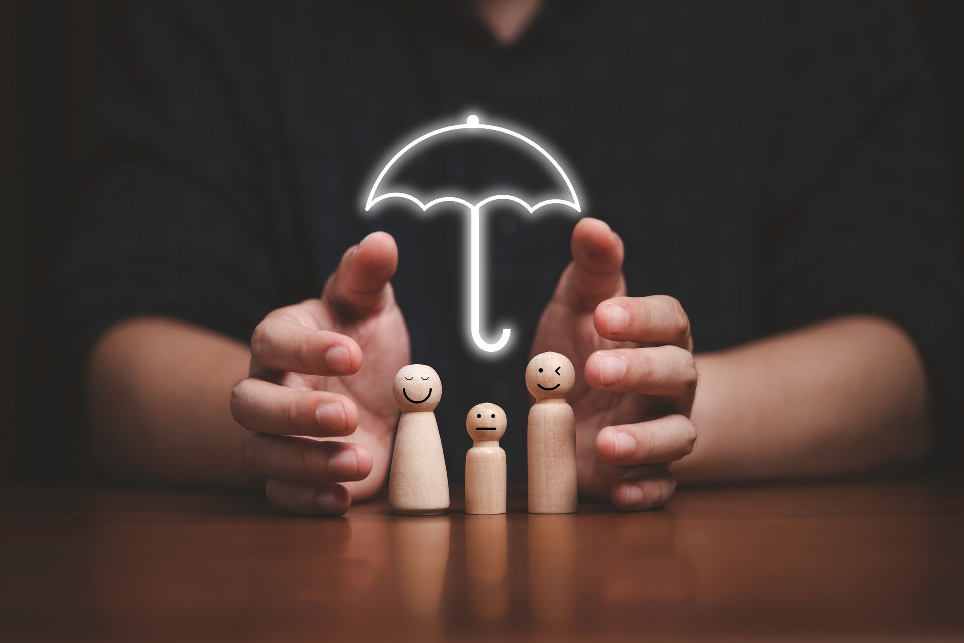 Hands shield wooden family figures under a glowing umbrella, symbolizing grief and loss counseling