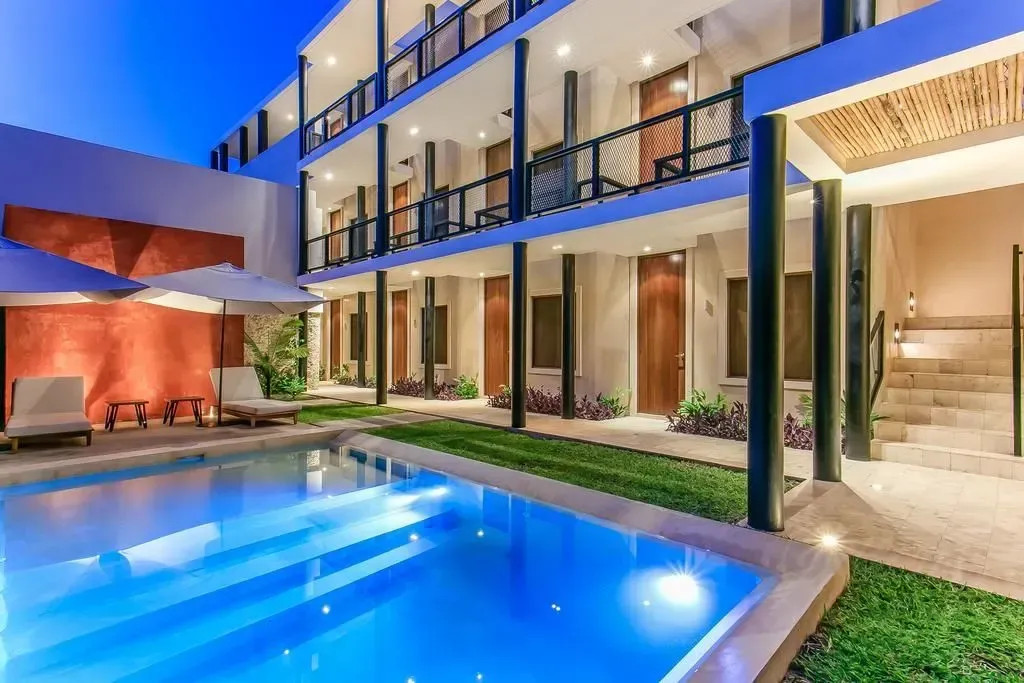 Modern luxury home with a lit blue pool, patio seating, and open-air balcony at dusk