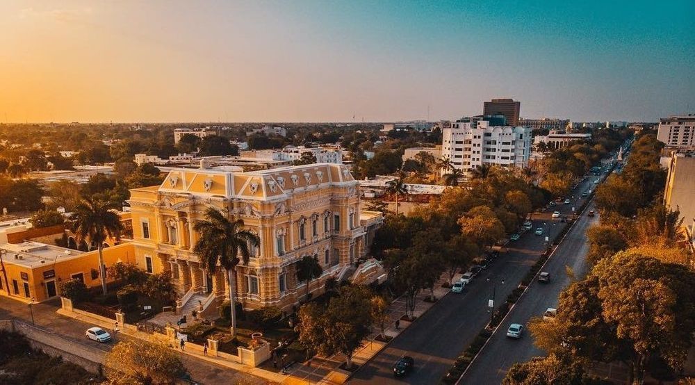 Sunset over a tree-lined city street with a historic building and low-rise buildings in the distance
