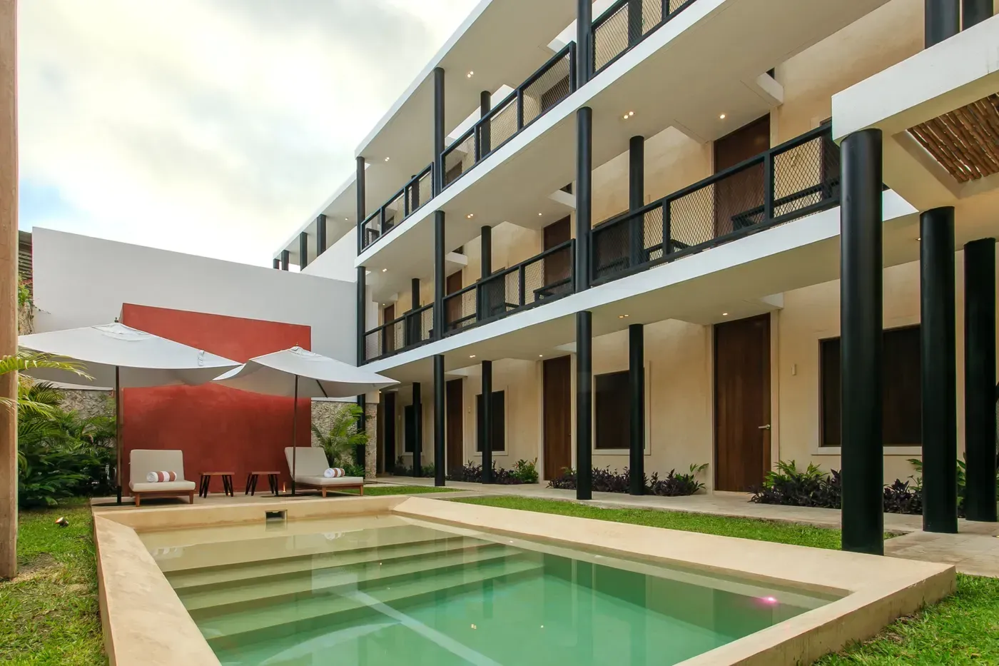 Modern apartment courtyard with a small pool, lounge chairs, and balconies along the building.