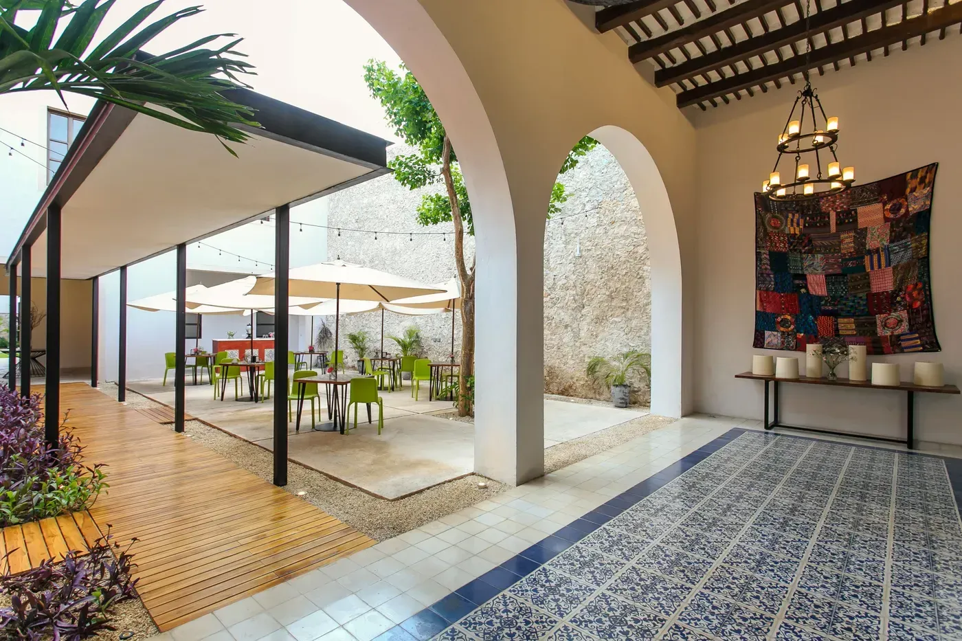 Covered courtyard with white arches, patterned tile floor, and outdoor tables under umbrellas beside a sunny patio.