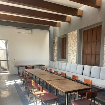 Modern dining room with long wooden table, gray banquette seating, and exposed ceiling beams