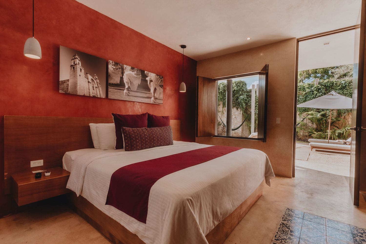 Modern bedroom with red accent wall, large bed, artwork, and open view to patio through glass doors