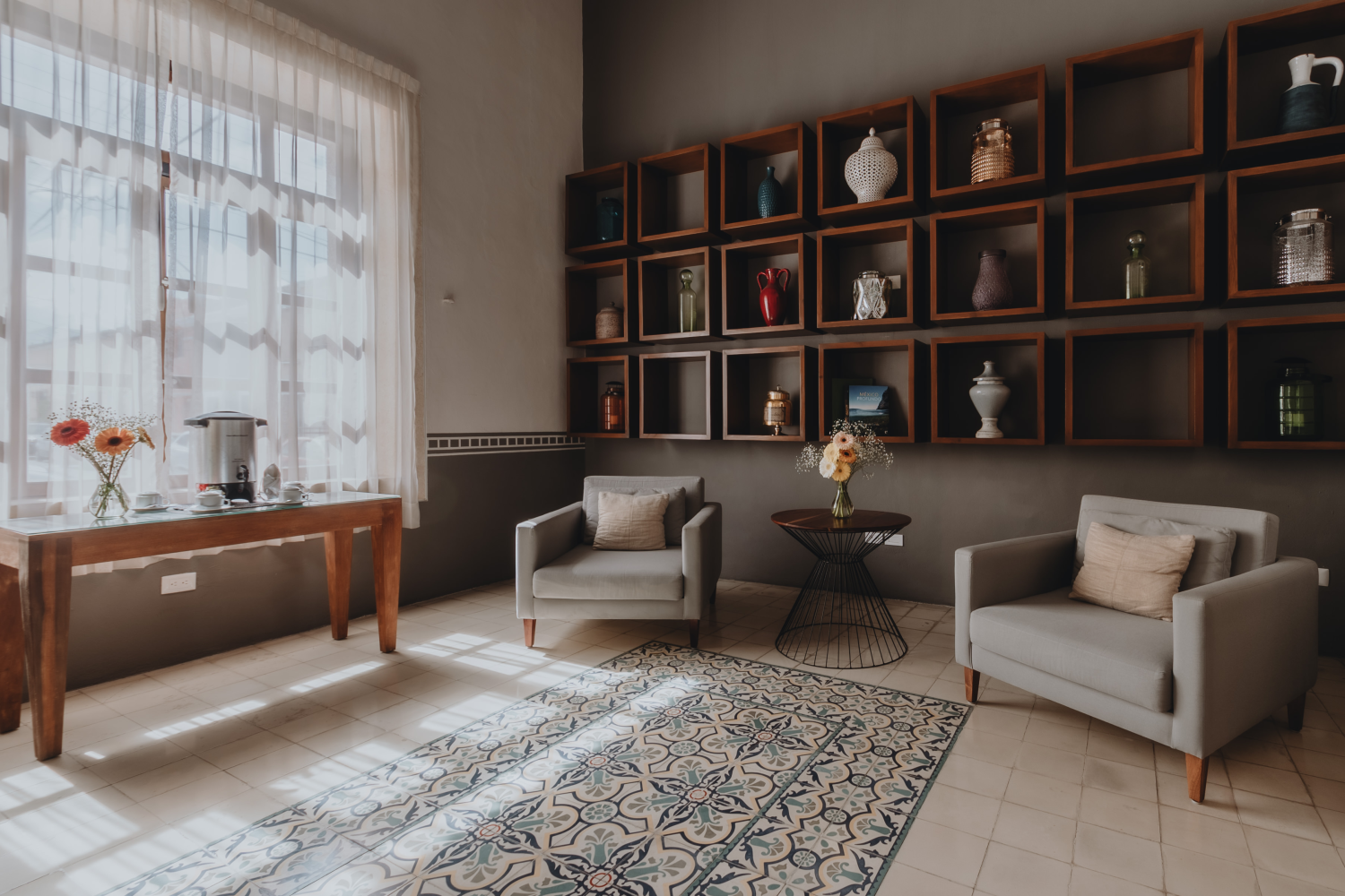 Elegant living room with beige armchairs, patterned rug, dark wood shelves, and a bright window seat