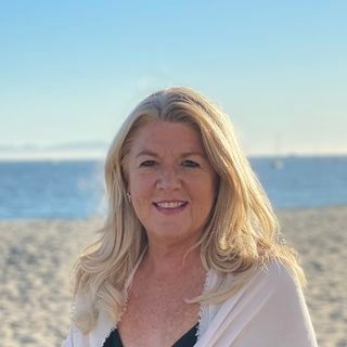 A woman is standing on a beach smiling at the camera.
